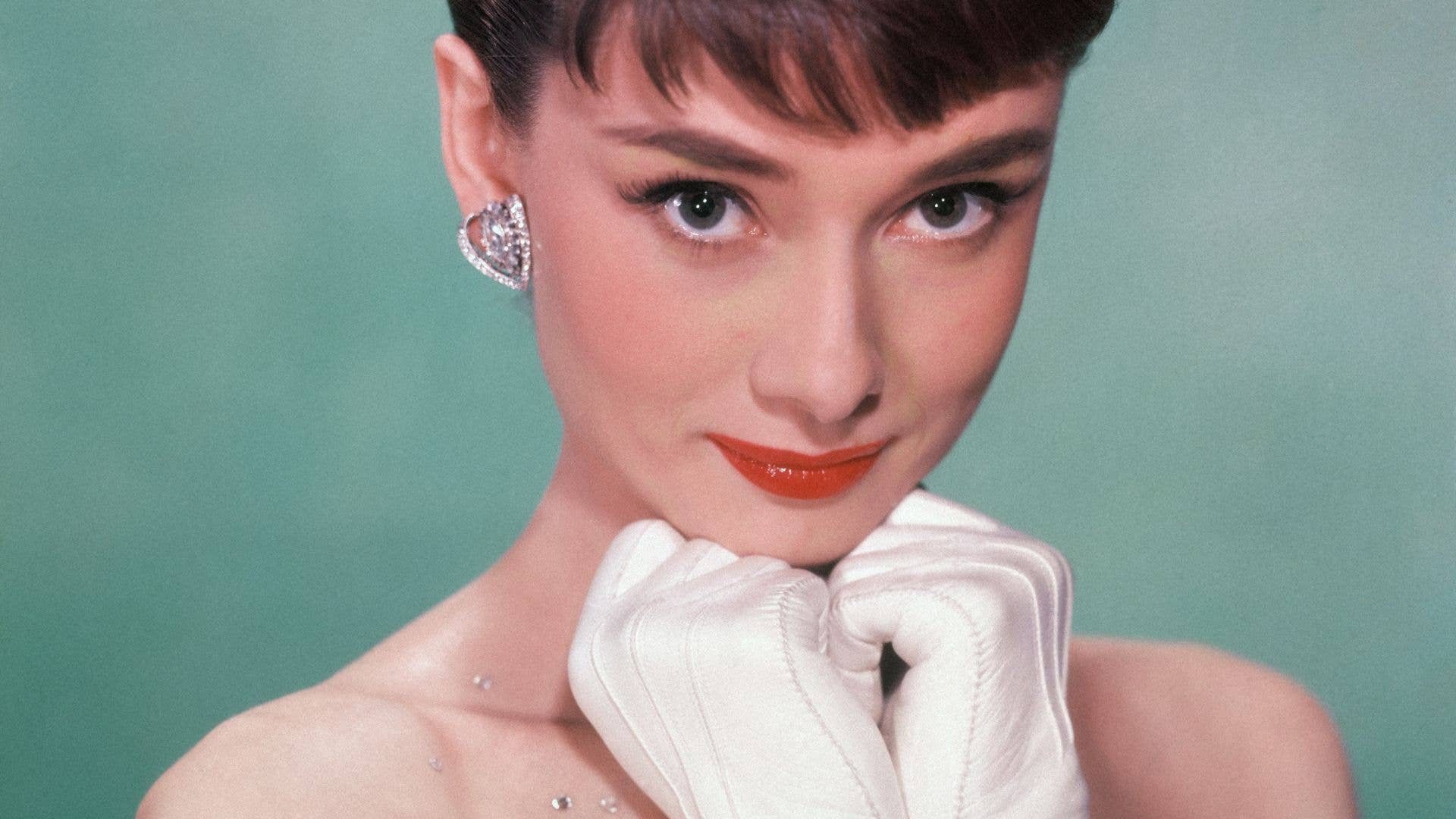 Portrait of Belgian-born American actress Audrey Hepburn (1929 - 1993) as she wears a strapless gown and holds white kid-gloved hands up to her chin
